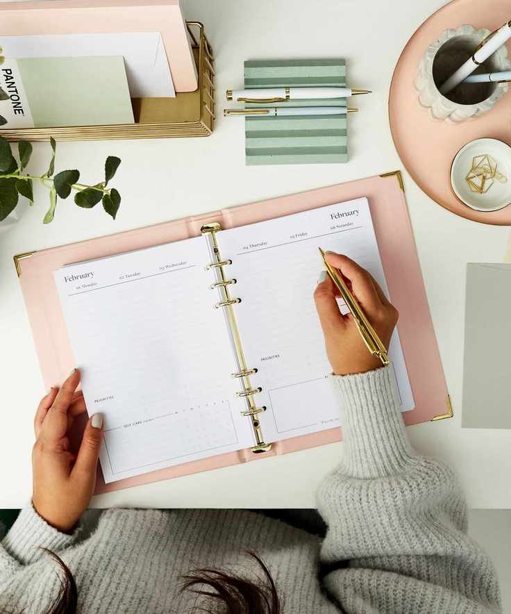 Someone writing in a Personalised Dream Plan Do Life Planner on a white desk surrounded by matching stationary